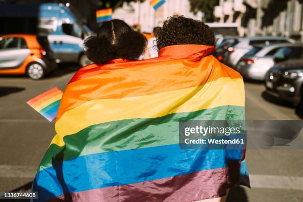 female friends wrapped in rainbow flag on sunny day - gay flag stock-fotos und bilder