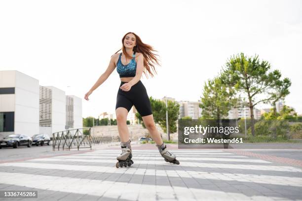 smiling young redhead woman skating on road in city - roller skate stock pictures, royalty-free photos & images