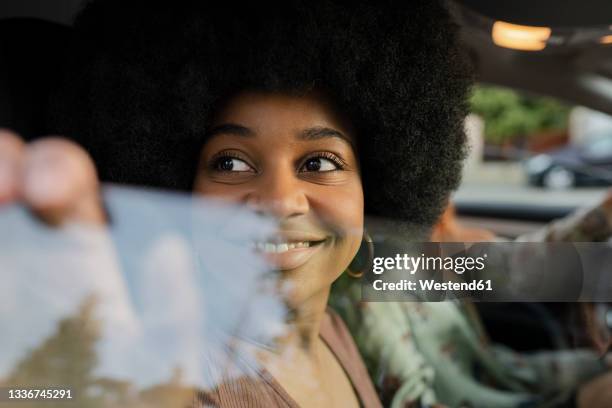 smiling afro woman looking through car window - car window stockfoto's en -beelden