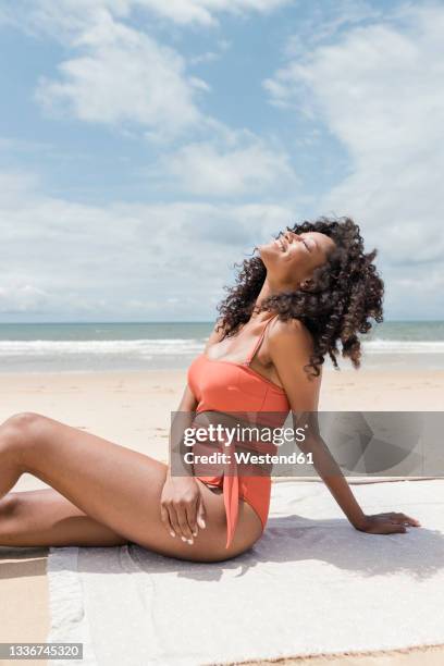 relaxed young woman sitting with head back on towel during sunny day - baño-de-pies fotografías e imágenes de stock