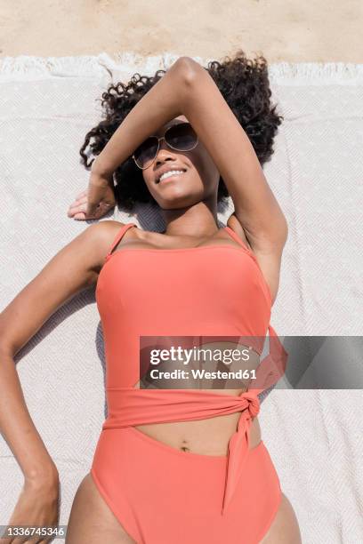 smiling young woman covering face with hand while lying at beach on sunny day - peach bath towels stock pictures, royalty-free photos & images