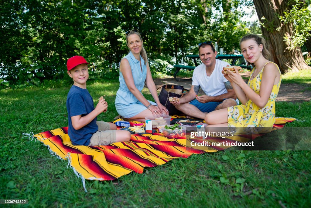 Portrait of family enjoying a picnic in public park in summer.