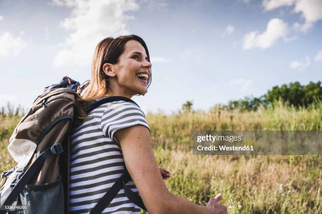 Cheerful woman with backpack looking away during sunny day