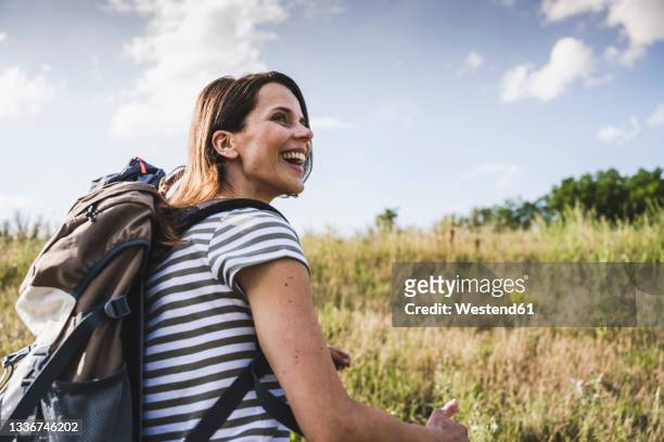 cheerful woman with backpack looking away during sunny day - mid adult woman germany stock pictures, royalty-free photos & images