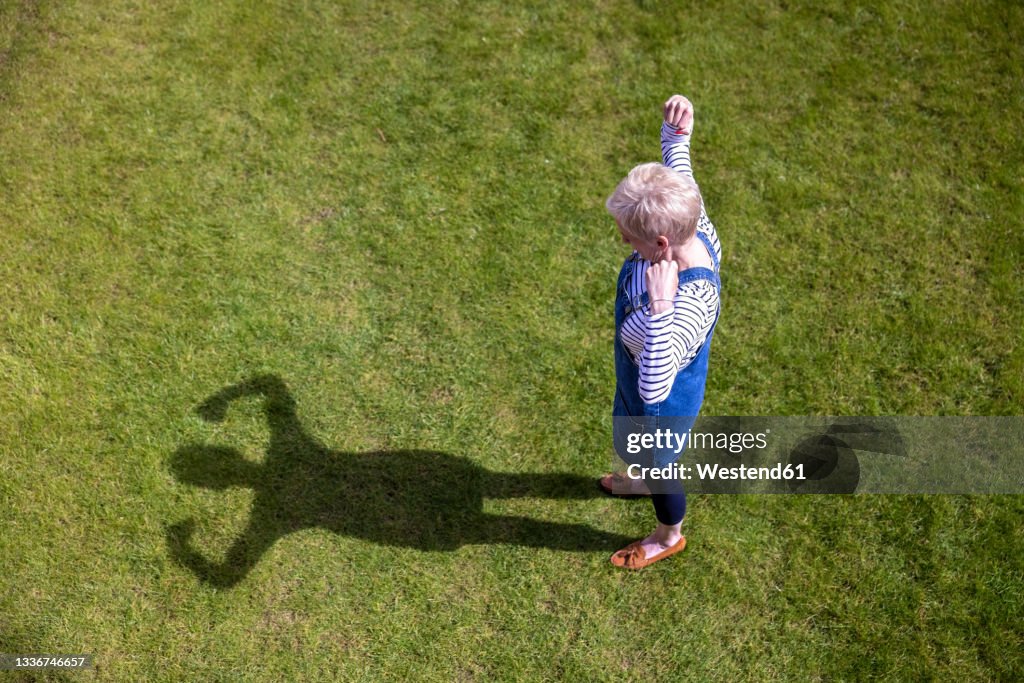 Woman flexing muscles while looking at shadow on grass