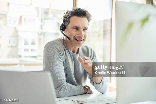 businessman with headset discussing through video call on computer in office - headset stock-fotos und bilder