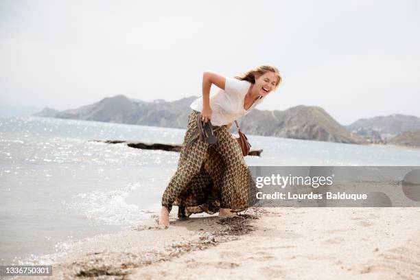 woman laughing out loud on the beach shore - knöcheltief im wasser stock-fotos und bilder