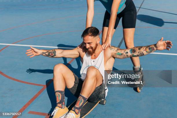 woman skating while pushing man sitting with arms outstretched on skateboard - roller en ligne photos et images de collection