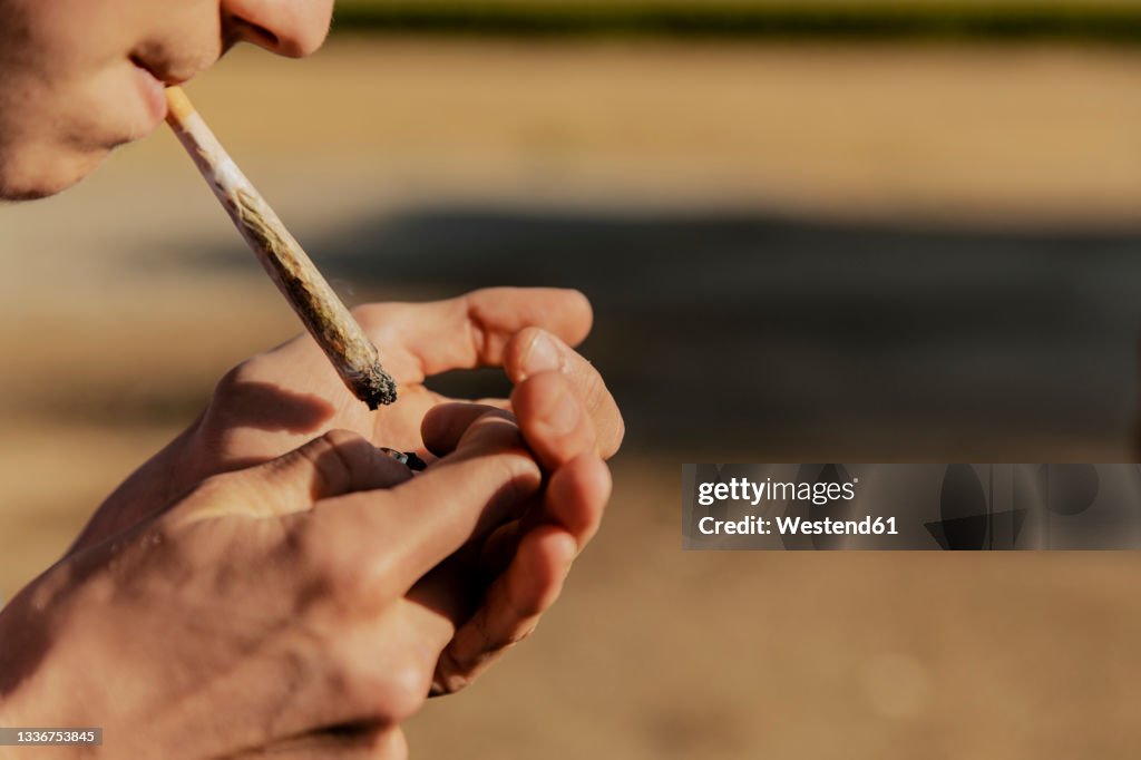 Teenage boy igniting marijuana joint during sunset