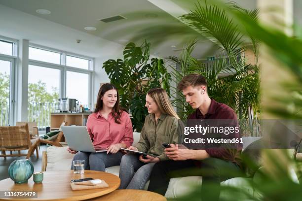 male professional using smart phone while sitting by female colleagues discussing in office - male teen tablet stock-fotos und bilder