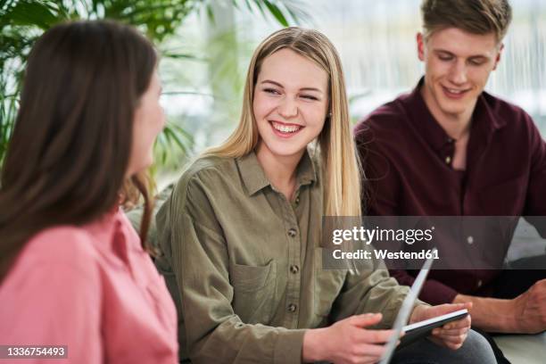 happy blond female intern discussing with businesswoman while sitting in office - aprendiz fotografías e imágenes de stock