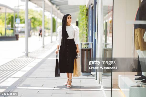 young woman with shopping bags looking at clothing store - arab shopping stockfoto's en -beelden