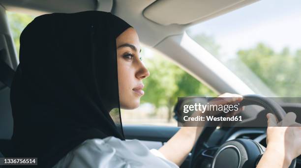 woman in hijab looking away while driving car - arab driving stock-fotos und bilder