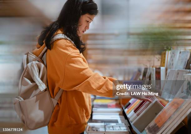 an asian woman with a backpack selects books from the library shelves - choosing a book stock pictures, royalty-free photos & images