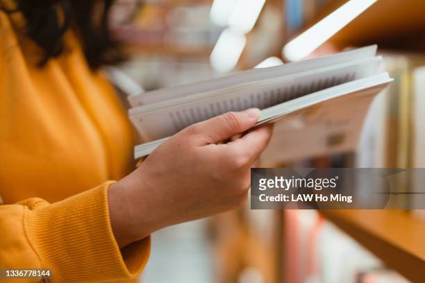 an asian woman flipping through a book in front of a bookshelf - open day 1 bildbanksfoton och bilder