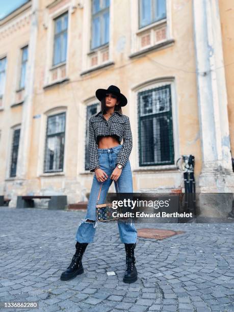 Jacqueline Barth wears a black felt / wool hat, a black and white houndstooth print pattern cropped long sleeves jacket, blue faded denim high waist...