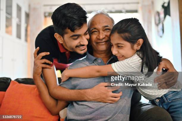 grandchildren embracing their senior grandfather lovingly - asiático e indio fotografías e imágenes de stock