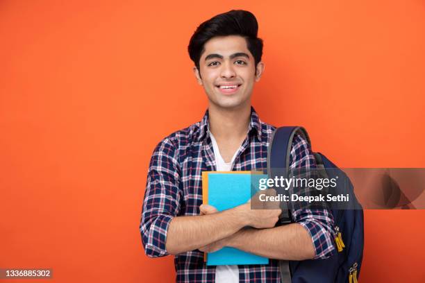 male teenage student in orange background stock photo - college student holding books stock pictures, royalty-free photos & images