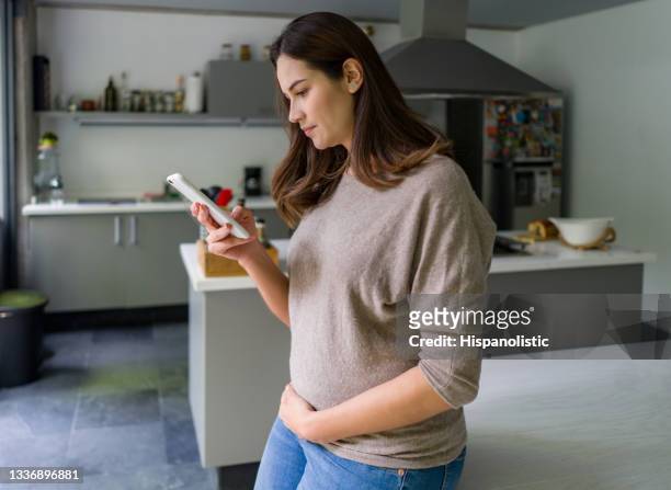 pregnant woman at home researching about pregnancy on her cell phone - text messaging mother stock pictures, royalty-free photos & images