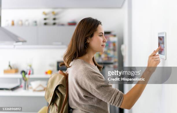 woman leaving her house and locking the door using a home automation system - huis interieur stockfoto's en -beelden