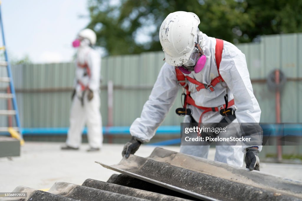 Safety is our top priority. Worker wearing full body protective clothing while working with the asbestos roof tiles.
