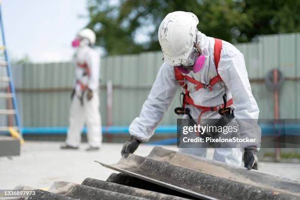 safety is our top priority. worker wearing full body protective clothing while working with the asbestos roof tiles. - asbestos stock pictures, royalty-free photos & images