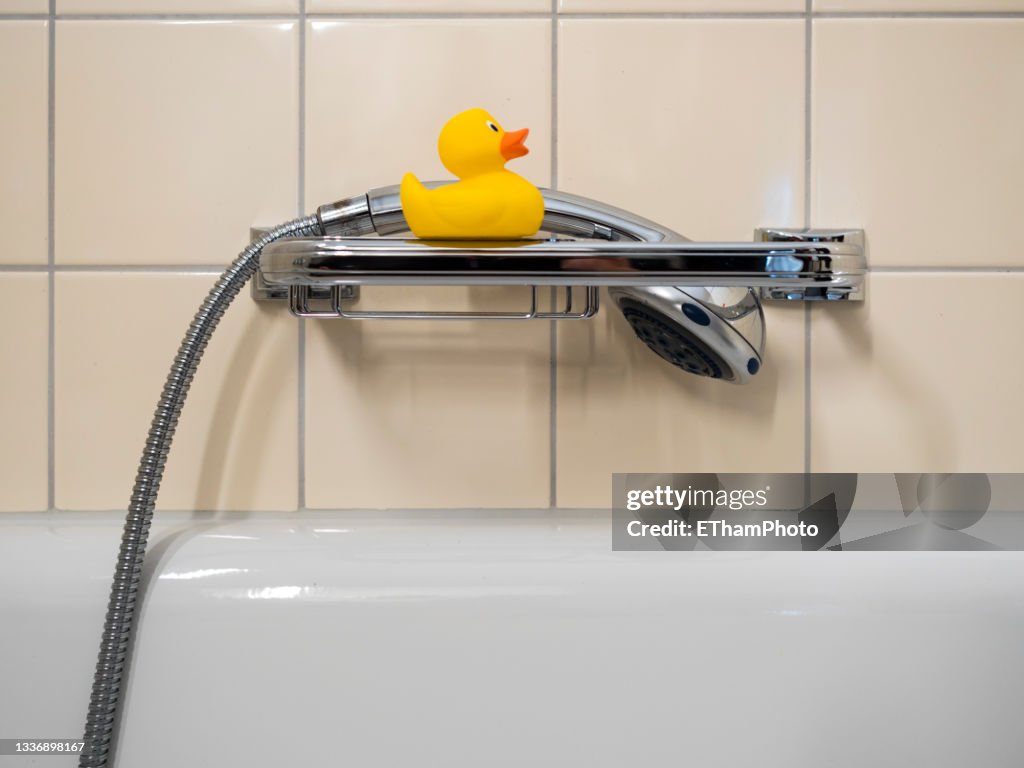 Yellow toy rubber duck sitting above bathtub
