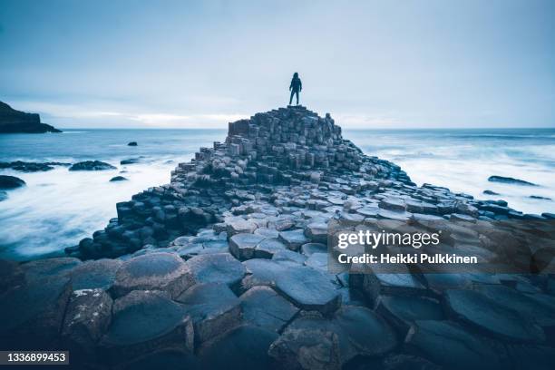 a person standing on the rocks by the sea at the giant's causeway, northern ireland - northern ireland foto e immagini stock