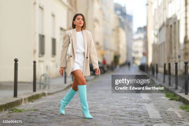 Alexandra Pereira wears a white t-shirt, white denim high waist shorts, a white shiny leather Cleo shoulder bag from Prada, a beige oversized blazer...