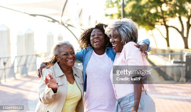 afroamerikanische seniorinnen lachen, umarmen sich im freien - dreiviertel vorderansicht stock-fotos und bilder