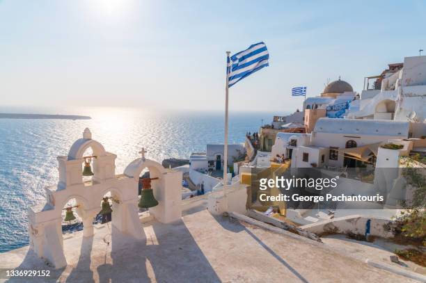 rooftop of greek orthodox church and the greek flag in oia, santorini - greece flag stock pictures, royalty-free photos & images