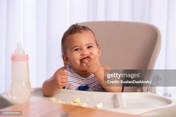 adorable bebé comiendo comida solo. - solido fotografías e imágenes de stock