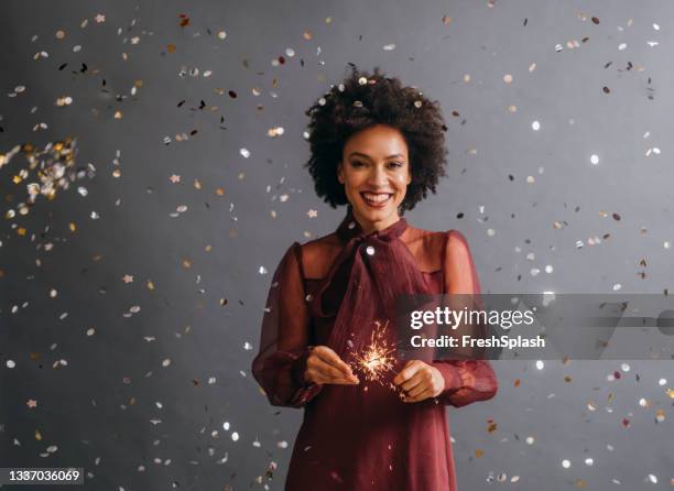 it's time to celebrate: portrait of a beautiful afro american woman holding a new year's sprinkler in confetti rain (gray background) - dress stockfoto's en -beelden