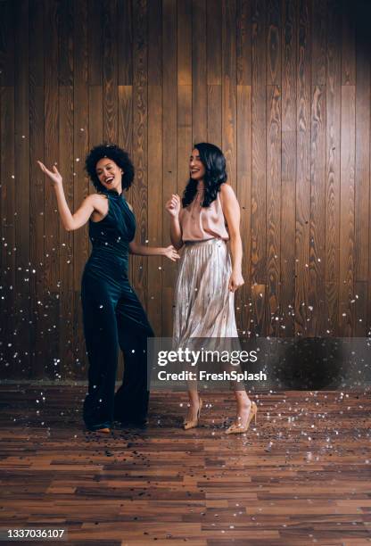 it's time to celebrate: two beautiful women dancing at a party in confetti rain - black jumpsuit stockfoto's en -beelden