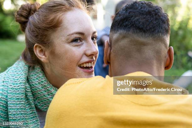 smiling young couple having fun while sitting in park - sussurrare foto e immagini stock