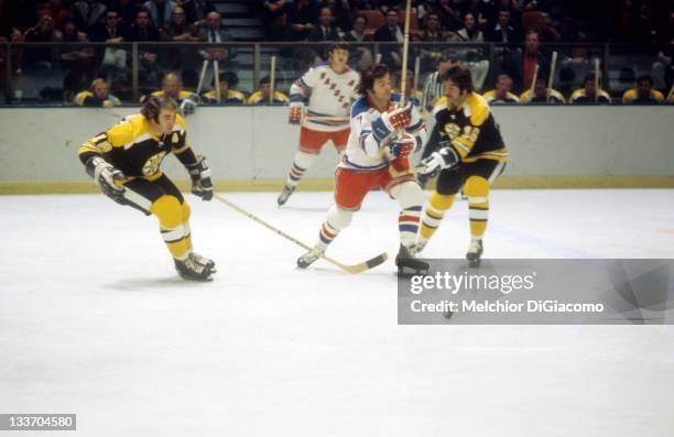 Ed Westfall of the Boston Bruins goes for the puck as his teammate Derek Sanderson slashes Rod Gilbert of the New York Rangers during their game...