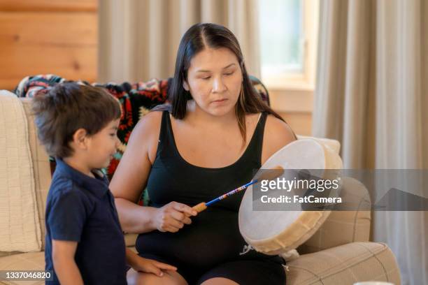 madre indígena tocando la batería para su hijo en casa - cultura de indios norteamericanos fotografías e imágenes de stock