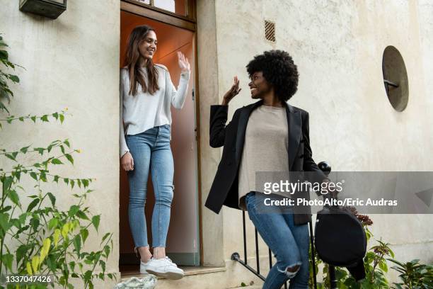 young female friends waving hands at doorstep - auf wiedersehen stock-fotos und bilder