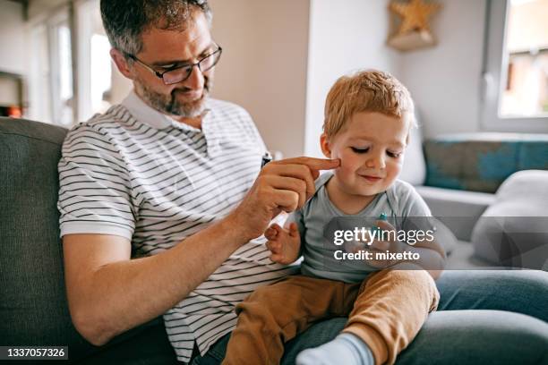 father carefully applying medical ointmen on his son face - beautiful baby bildbanksfoton och bilder