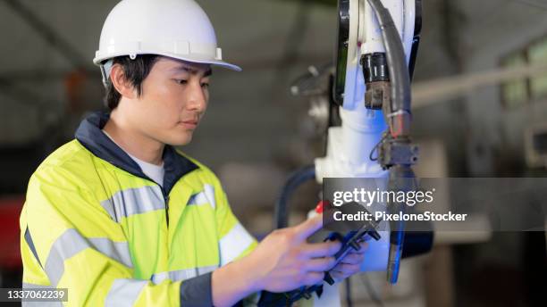 male industrial engineer holding the digital controller standing beside the robotic welding machine in the metal factory. - digital devices beside each other bildbanksfoton och bilder