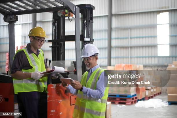 asian chinese warehouse supervisor manager signing documents receiving goods from his coworker operating forklift working in industry factory - loader reading stock pictures, royalty-free photos & images