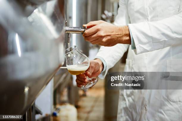 senior supervisor beim einschenken eines glases bier in der brauereianlage - brauerei stock-fotos und bilder