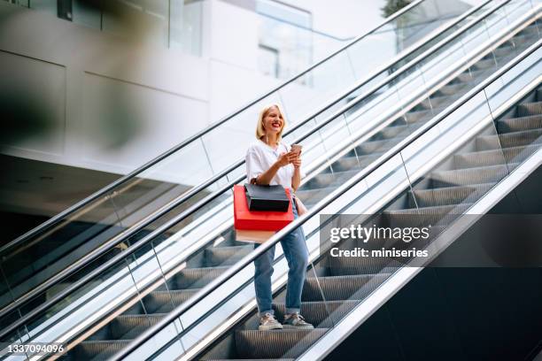 belle femme souriante utilisant un téléphone portable debout sur l’escalator - escalator photos et images de collection