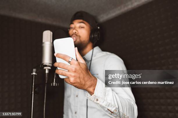 afro american rapper man, using smartphone in recording studio with microphone - producent stock-fotos und bilder