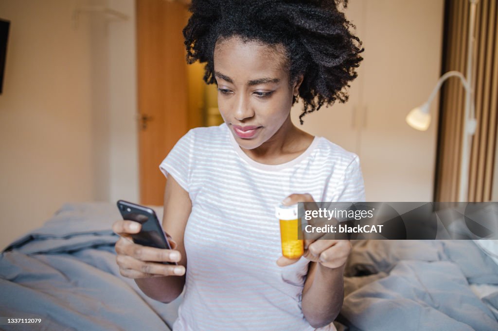 African American woman is looking for information on the internet about the medicine she is holding in her hand