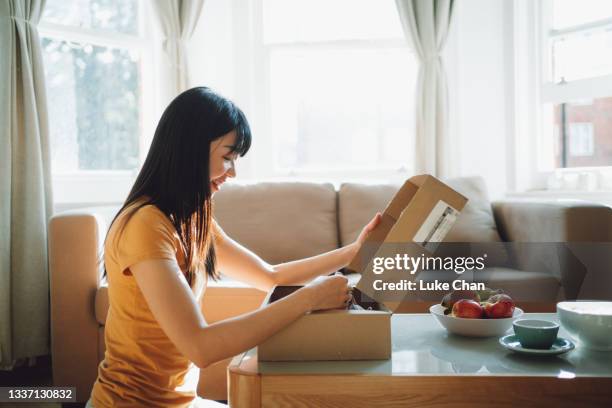 smiling young woman opening a delivery box in the living room - opening a box stockfoto's en -beelden