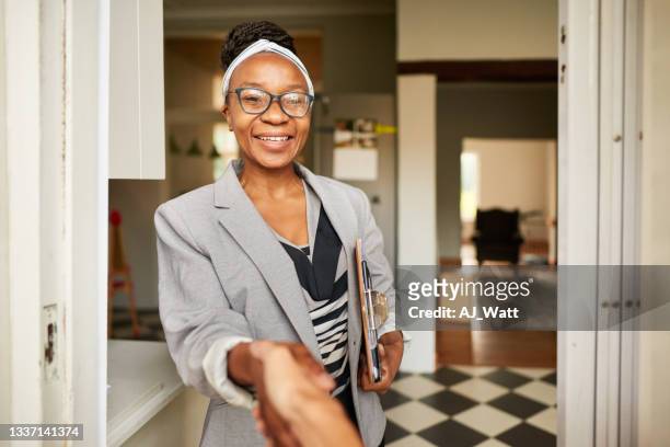smiling real estate agent shaking hands with a client at a house entrance - african pov stock pictures, royalty-free photos & images