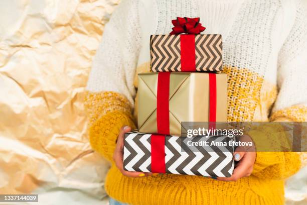 heap of different gift boxes in hands of woman in white-yellow sweater against crumpled paper background. christmas celebration and new year coming concept.  front view - three year stock pictures, royalty-free photos & images