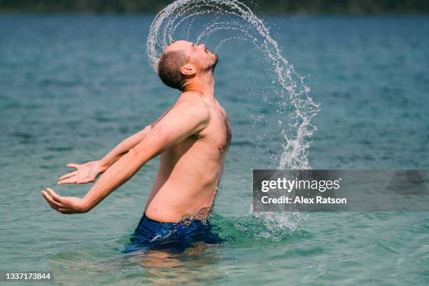 man whips head from under the water spraying water into the air - alex pix photos et images de collection