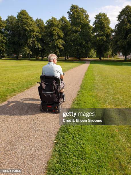 male riding his mobility scooter in public park in shrewsbury shropshire, enjoying the freedom and independence the vehicle gives him as he is unable to walk. - mobility scooters stock pictures, royalty-free photos & images